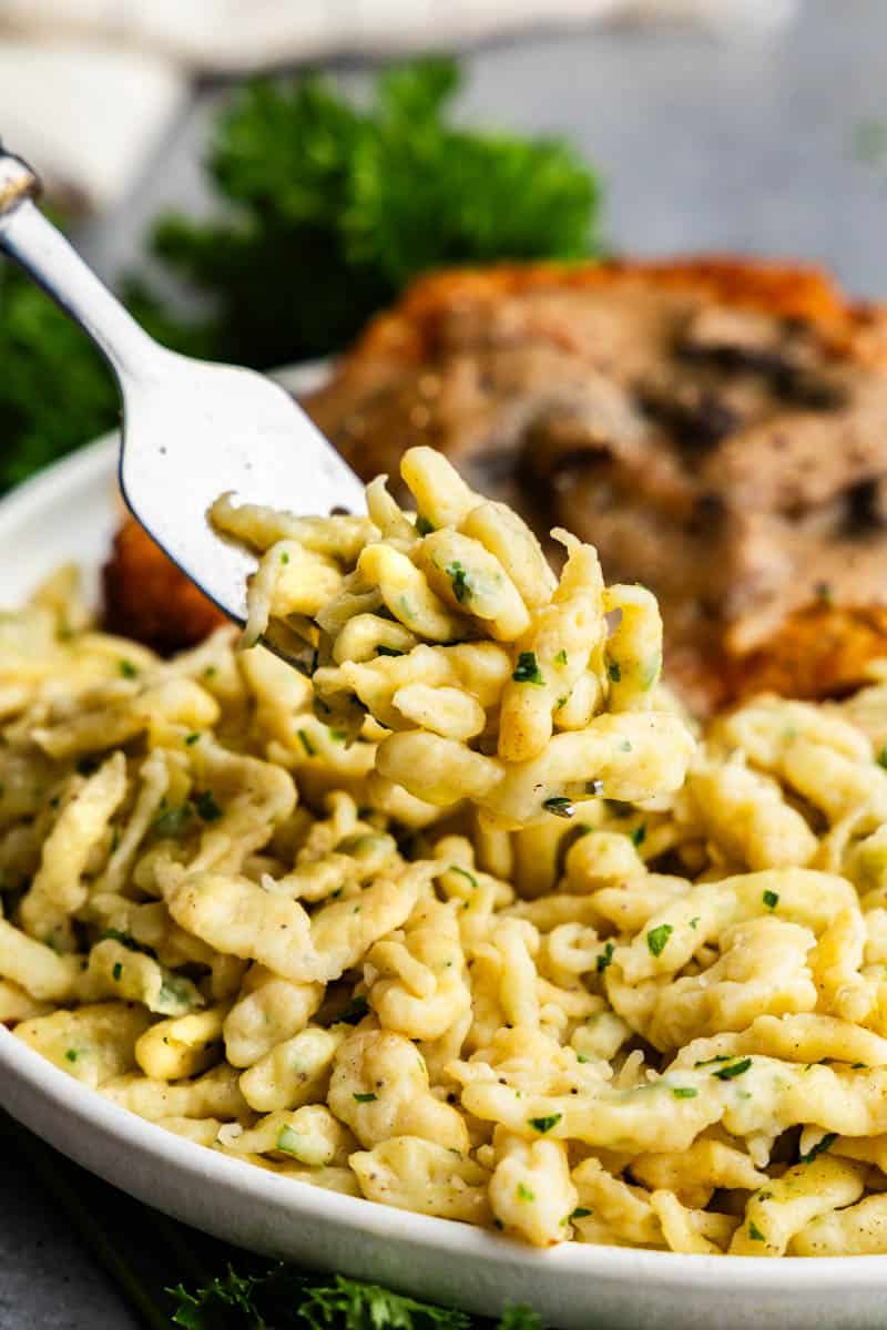 A fork lifting a bite of Granny's German spaetzle from a plate.