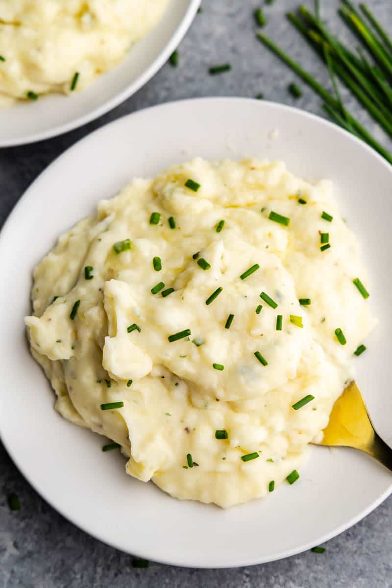 An overhead view of a plate filled with a serving of herbed butter mashed potatoes with a fork set in for eating.