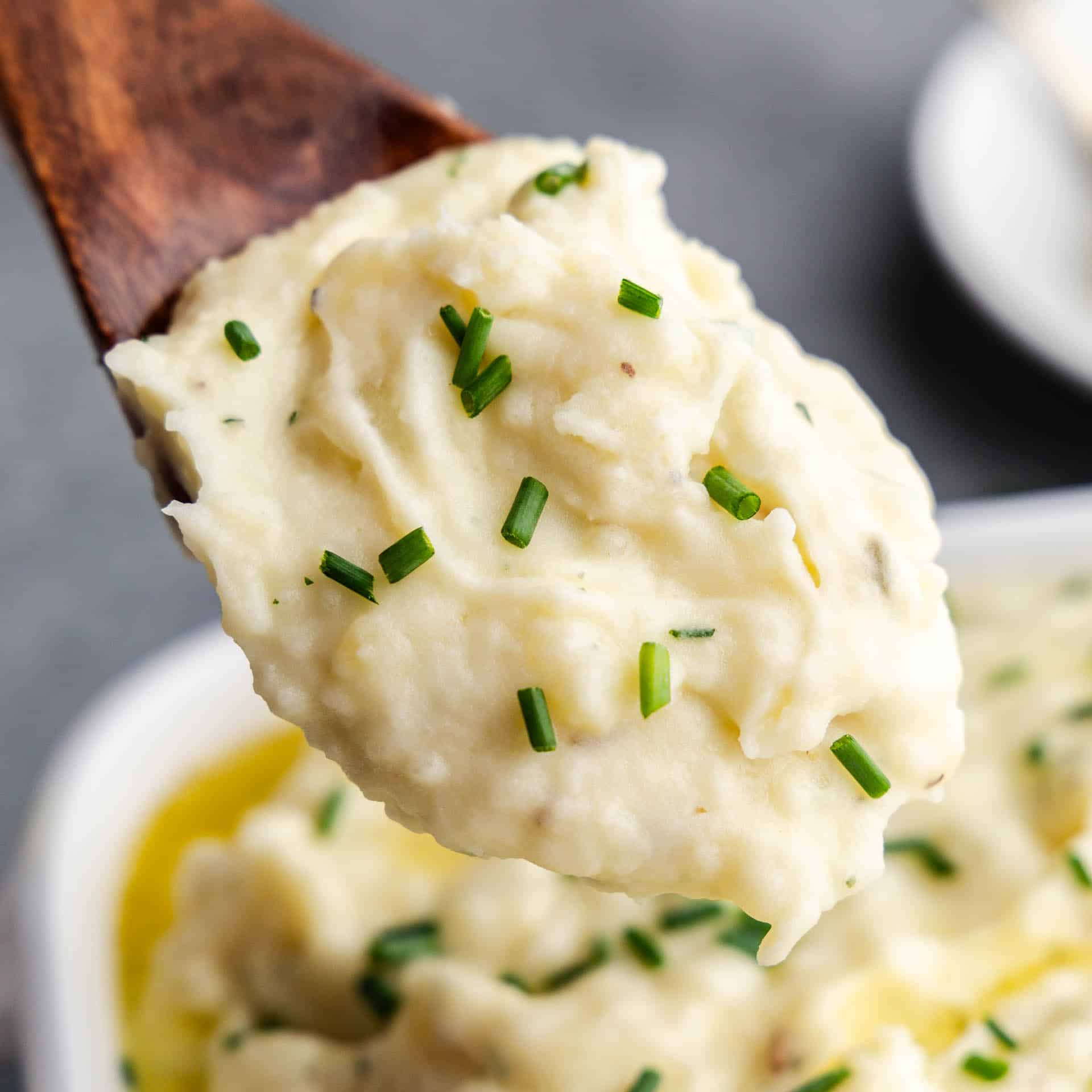 A close up of a wooden spoon holding a scoop of herbed butter mashed potatoes.