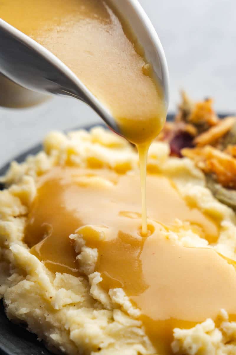 A gravy boat pouring gravy onto a plate of mashed potatoes.