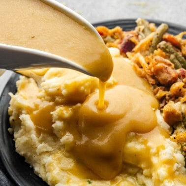 A gravy boat pouring gravy onto a plate of mashed potatoes and green bean casserole.