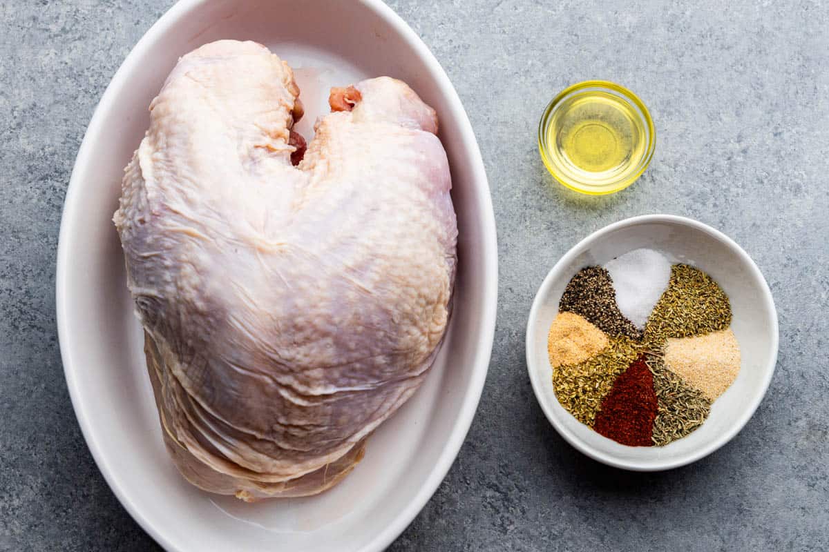 An overhead view of a raw turkey breast and ingredients need to make oven roasted turkey breast.