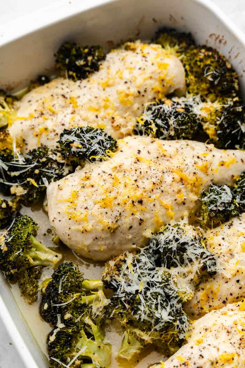 A close up view of chicken breasts surrounded by broccoli and topped with lemon zest and parmesan cheese.