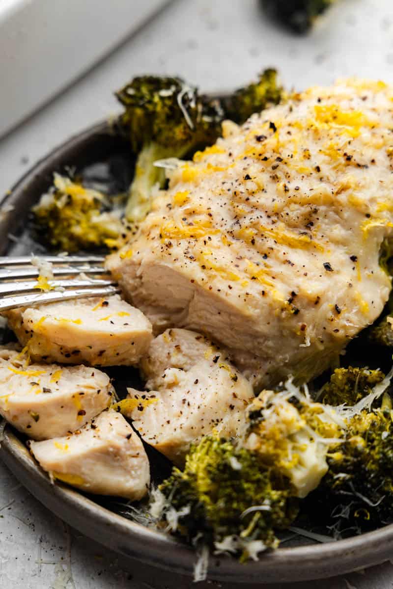 A plate of lemon garlic chicken and broccoli with pieces of the chicken sliced and ready to take a bite.