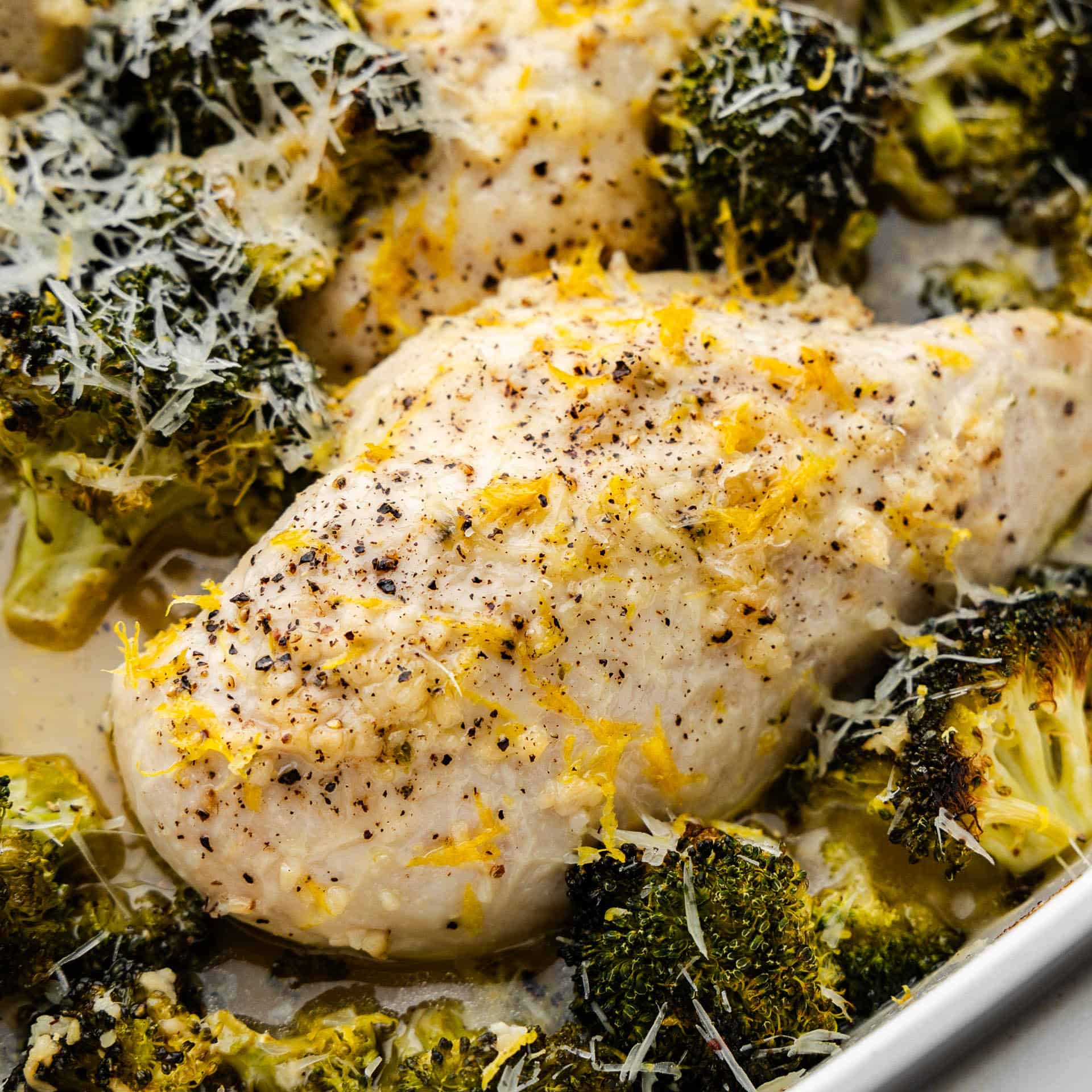 A close up view of a chicken breast with lemon zest surrounded by broccoli.