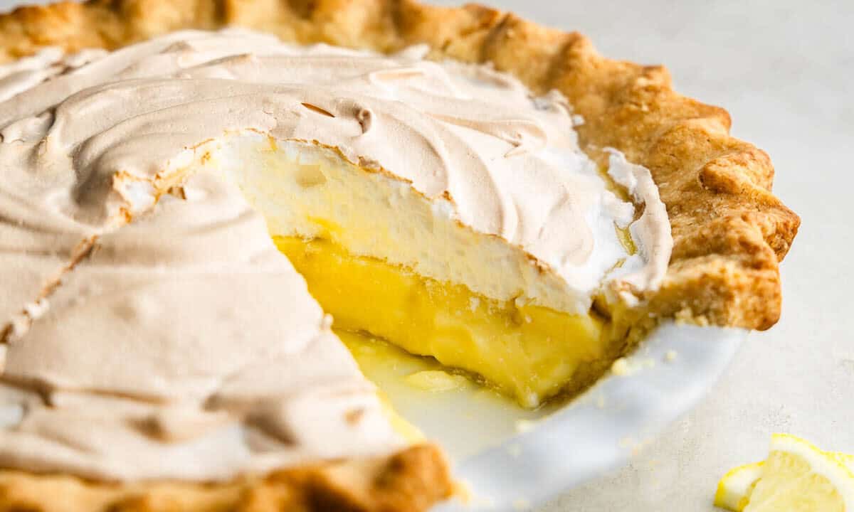 A lemon meringue pie in a white pie plate with a slice taken out.