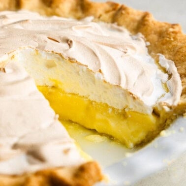 A lemon meringue pie in a white pie plate with a slice taken out.