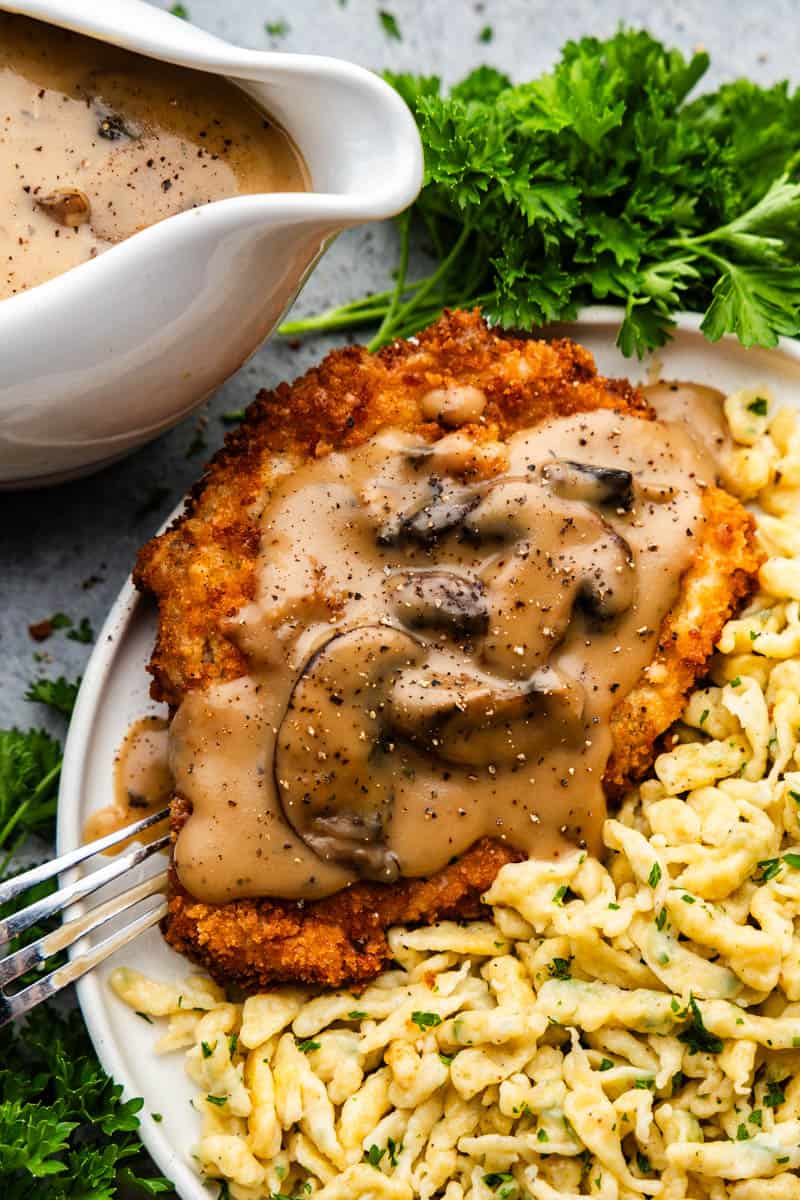 An overhead view of a plate of German schnitzel and spaetzle, topped with mushroom gravy.