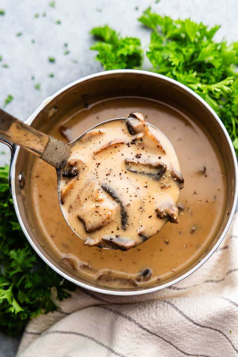 An overhead view with a ladle in a saucepan serving mushroom gravy.