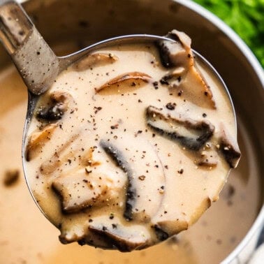 An overhead view of a saucepan filled with mushroom gravy, with a ladle lifting a scoop out of the pan.