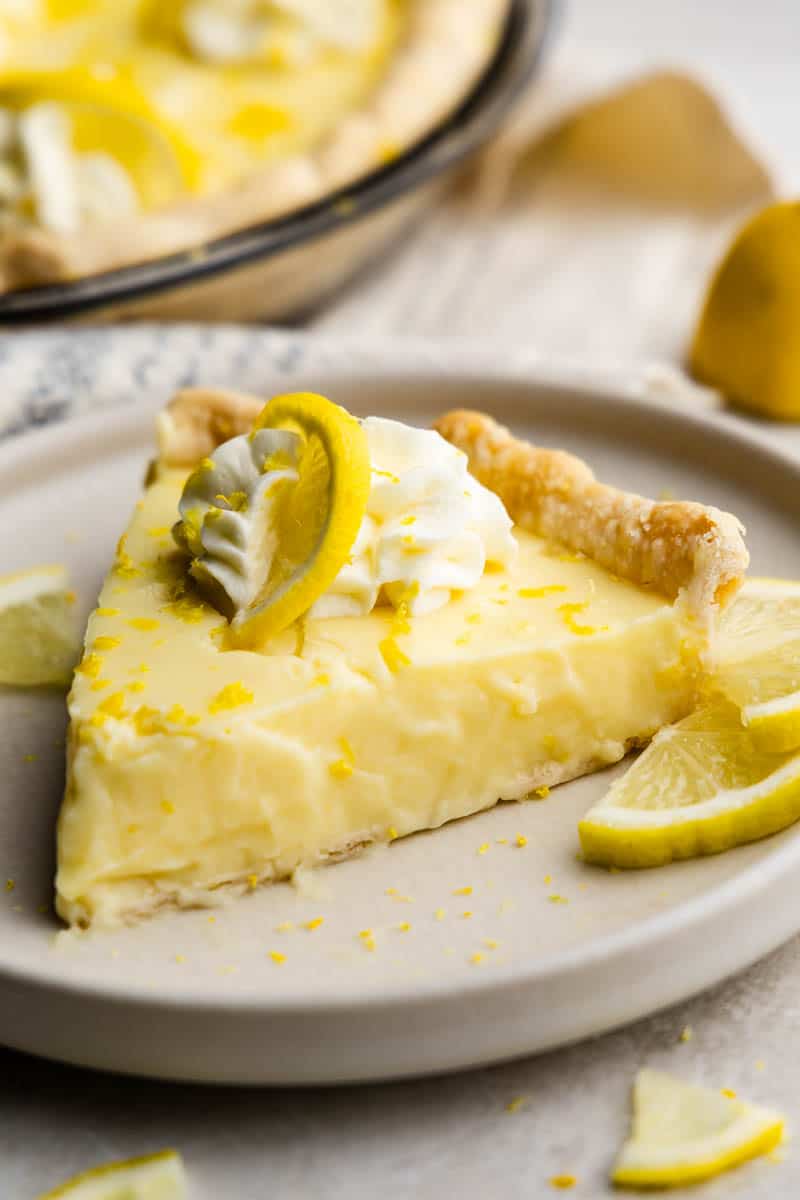 A slice of creamy lemon pie on a plate, set next to slices of fresh lemon.