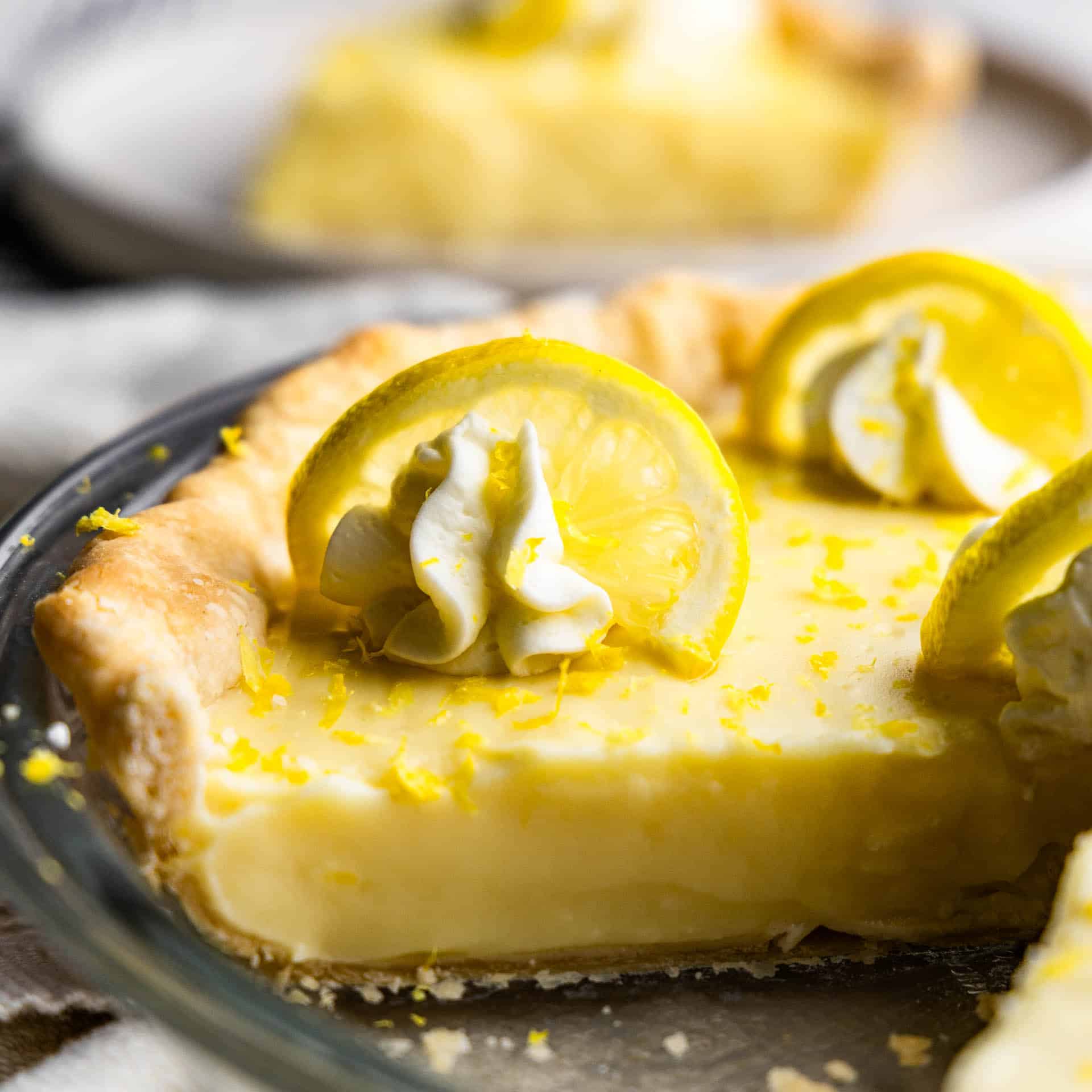 A close up side view of a glass pie dish holding an old fashioned creamy lemon pie, with a slice missing.