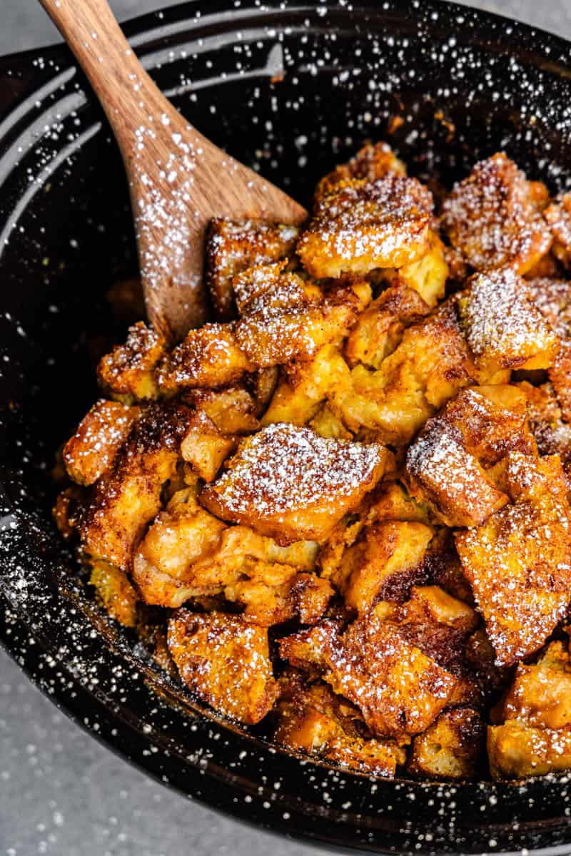 Overhead view of slow cooker crock filled with pumpkin French toast casserole. A wooden spoon is attached.