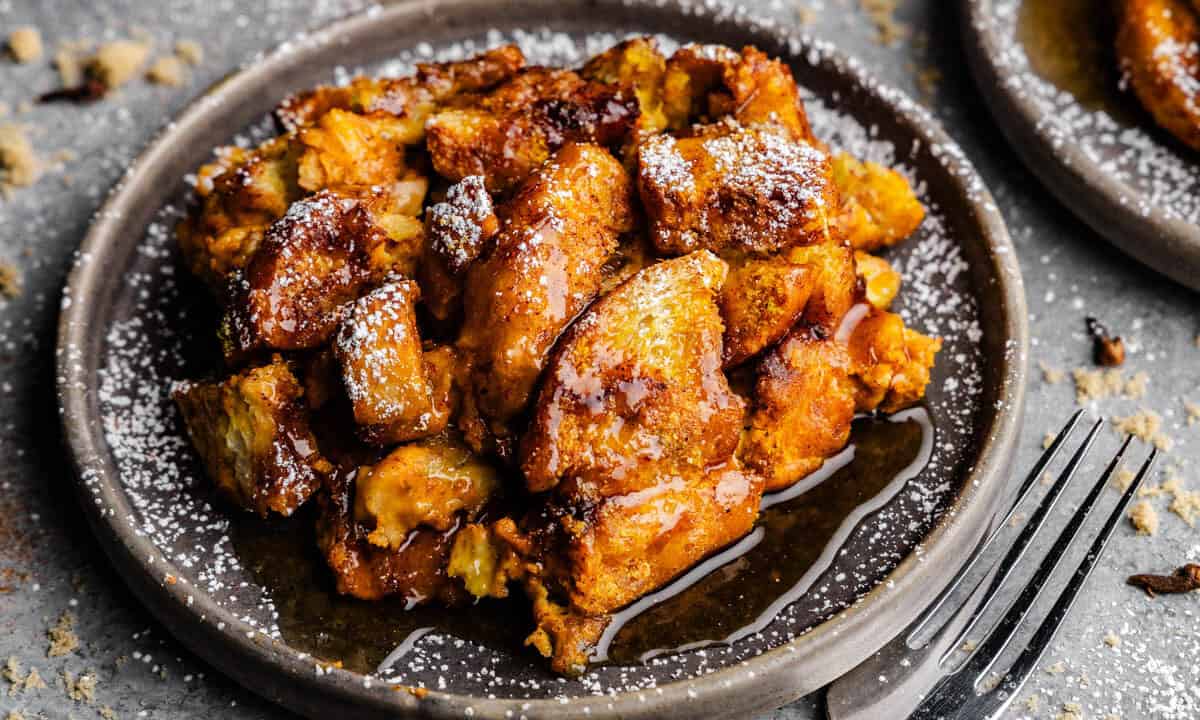 A gray plate of pumpkin french toast casserole, drizzled with maple syrup and dusted with powdered sugar.