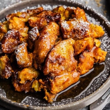 A gray plate of pumpkin french toast casserole, drizzled with maple syrup and dusted with powdered sugar.