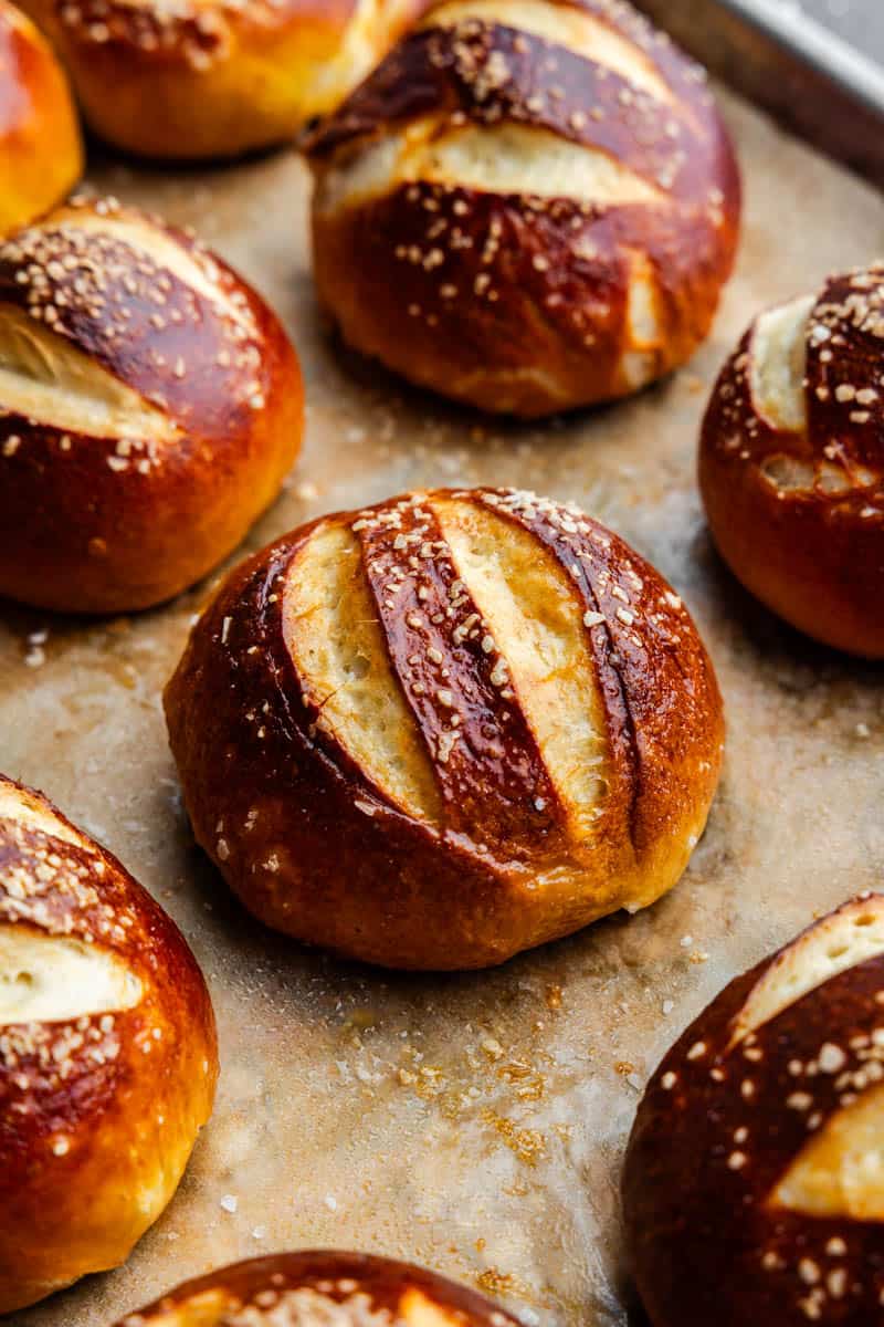 Homemade pretzel rolls on a parchment lined baking sheet, fresh out of the oven.