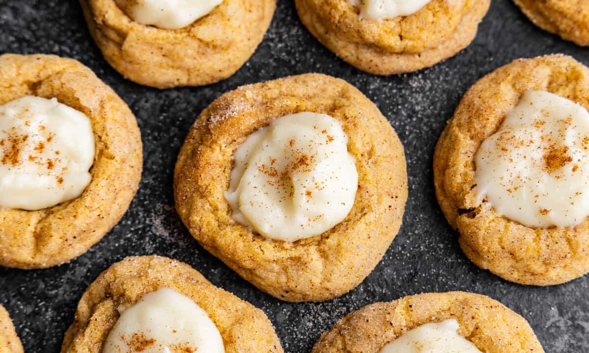 An overhead view of pumpkin cheesecake thumprint cookies on a dark platter.