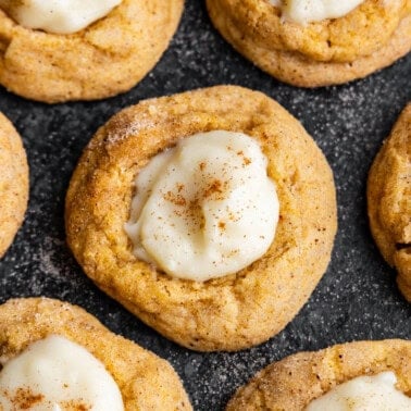 An overhead view of pumpkin cheesecake thumprint cookies on a dark platter.