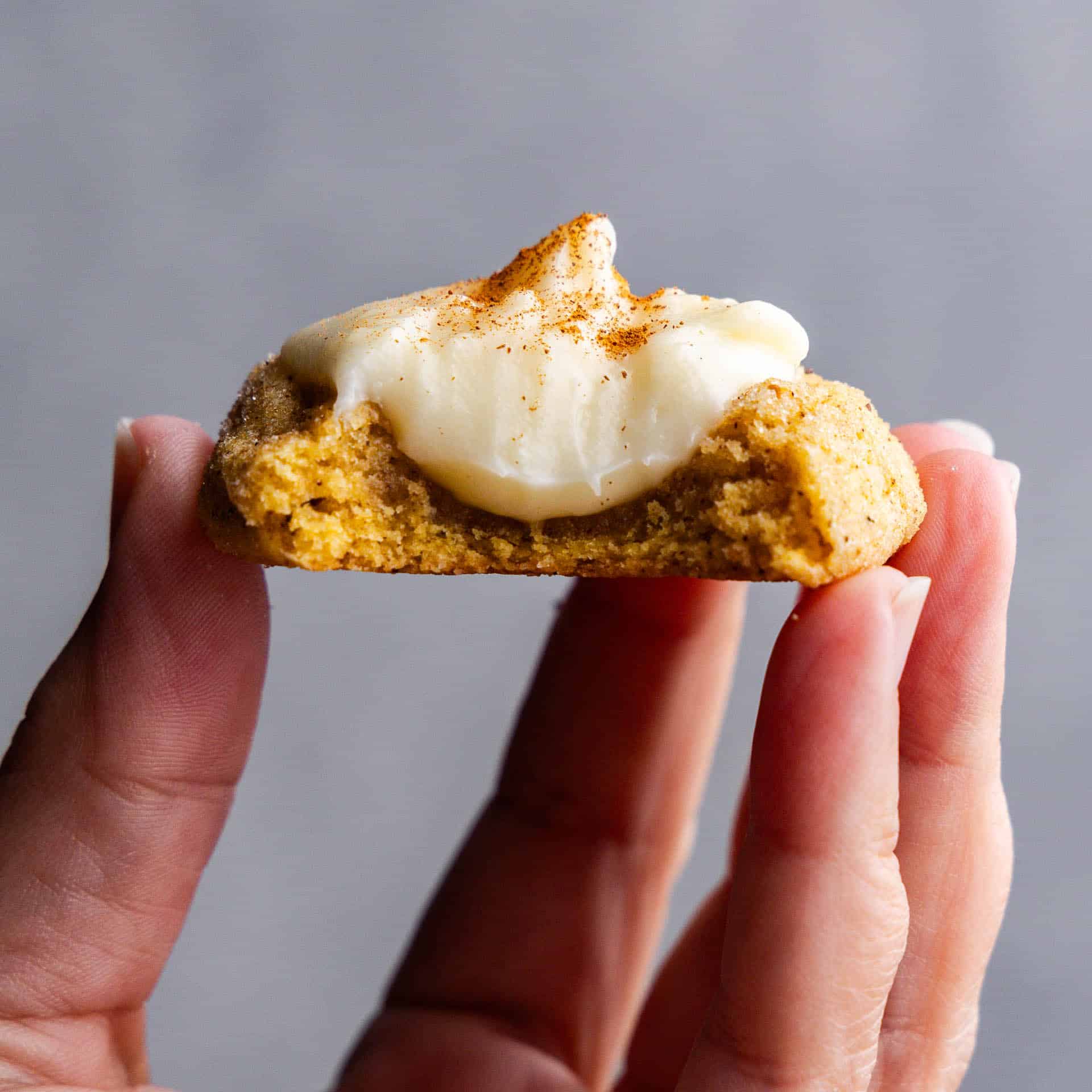 A hand holding a pumpkin cheesecake thumbprint cookie that has been bitten into.