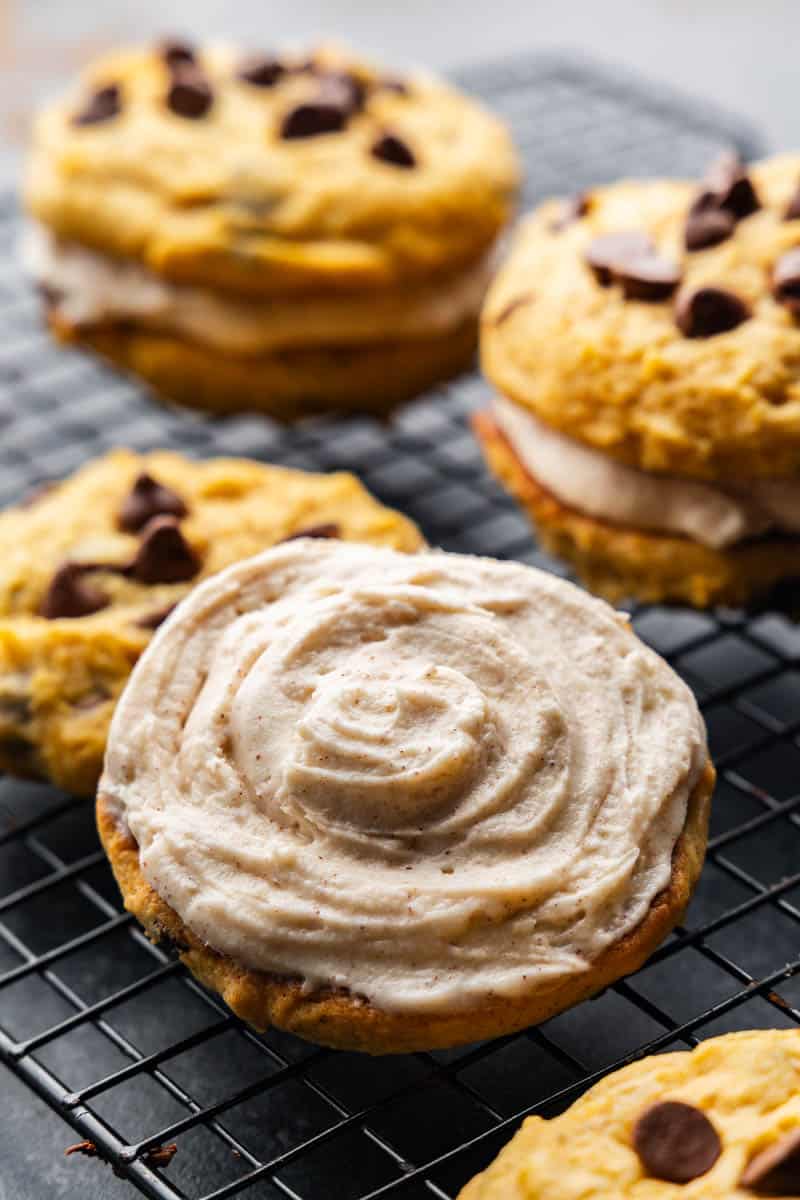 Close up view of a pumpkin chocolate chip cookie topped with cream filling next to other pumpkin sandwich cookies.