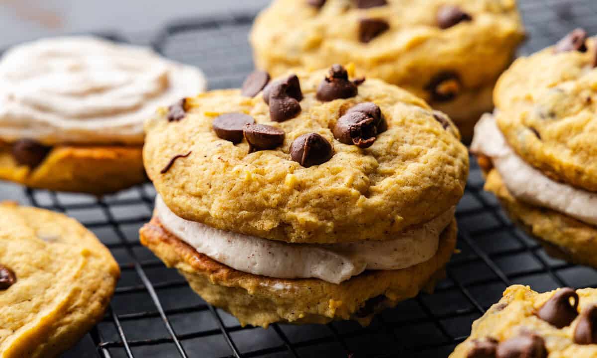 A close up view of several pumpkin chocolate chip cookie sandwiches on a cooling rack.