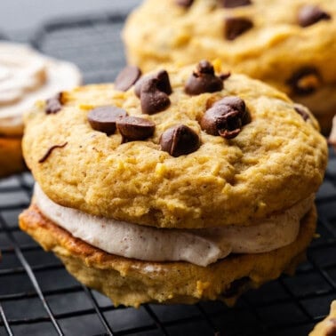 A close up view of several pumpkin chocolate chip cookie sandwiches on a cooling rack.