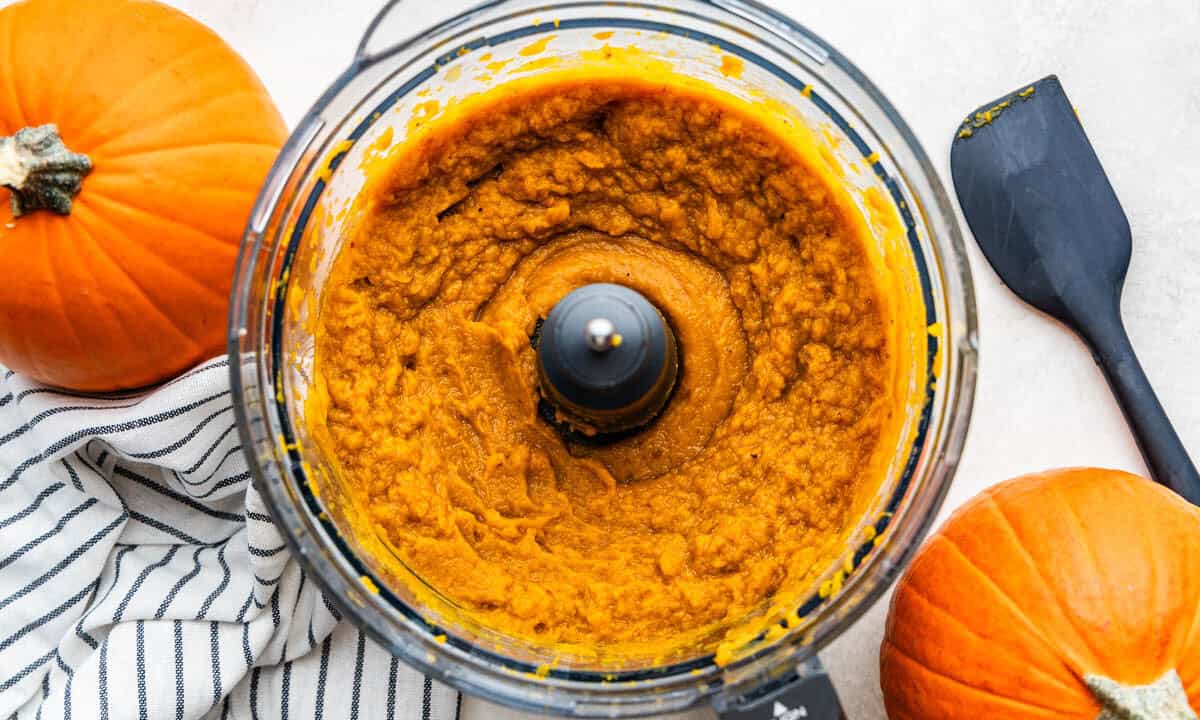 An overhead view into a food processor filled with pumpkin puree.