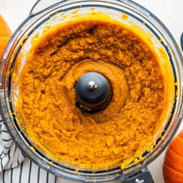 An overhead view into a food processor filled with pumpkin puree.