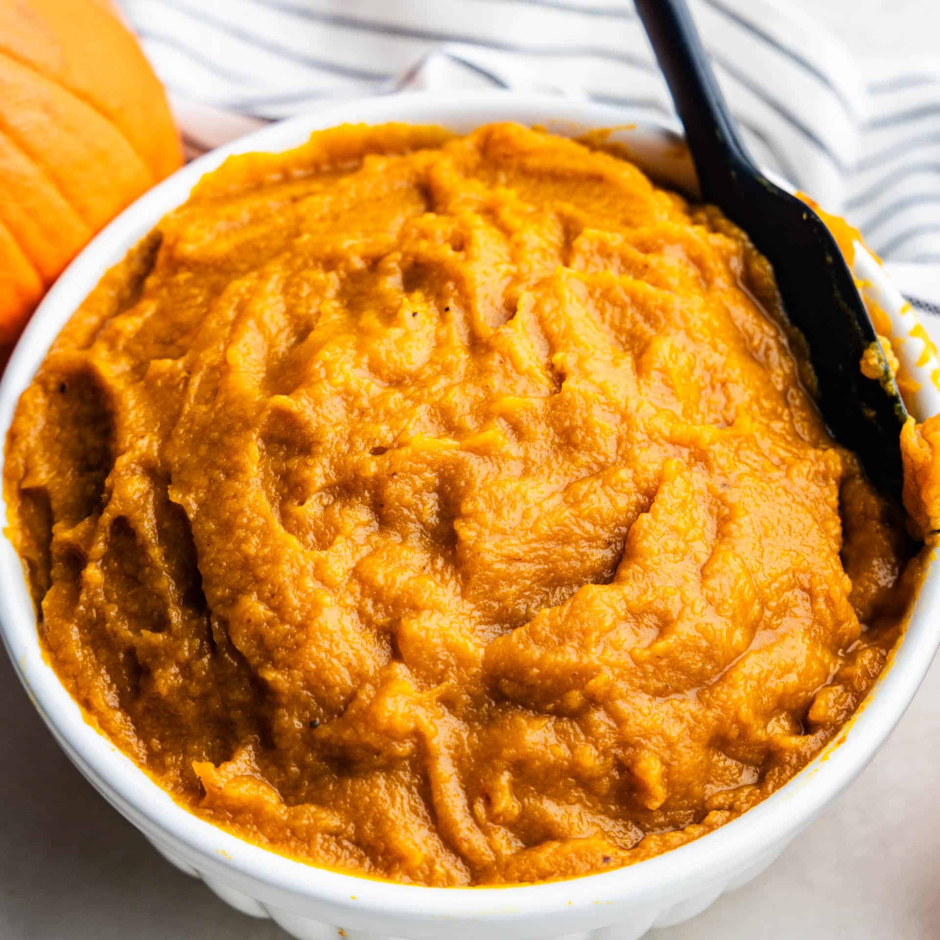 A close up view of a bowl of pumpkin puree with a spatula ready to scoop some out.