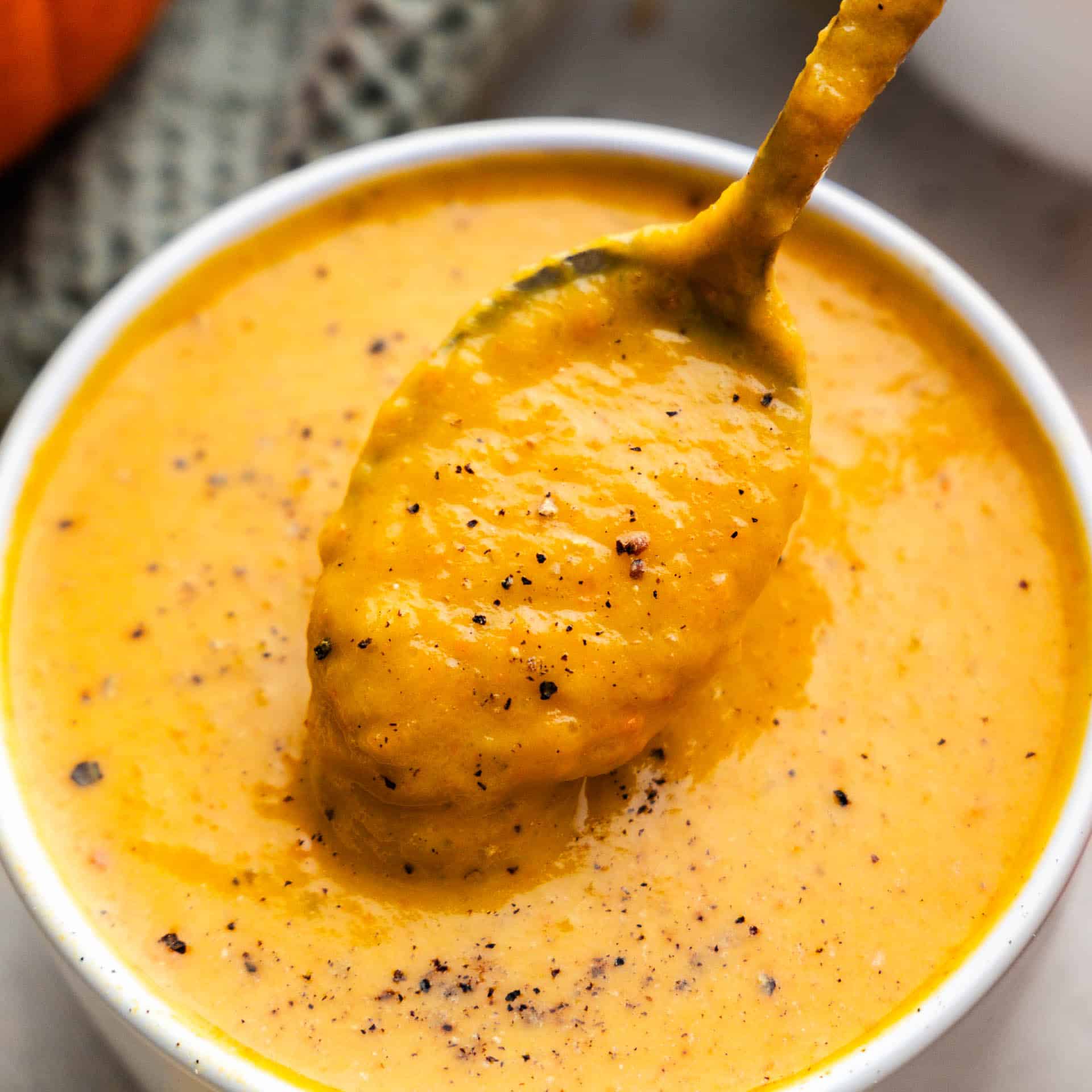 A close up view of a bowl of pumpkin soup with a spoon dishing out a bite.