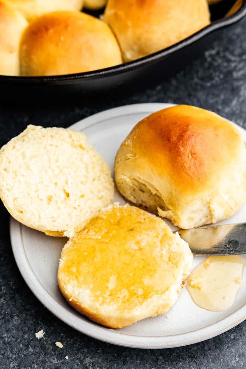 A close up of a plate holding skillet rolls with one split open and the middle of it smothered in butter and honey.