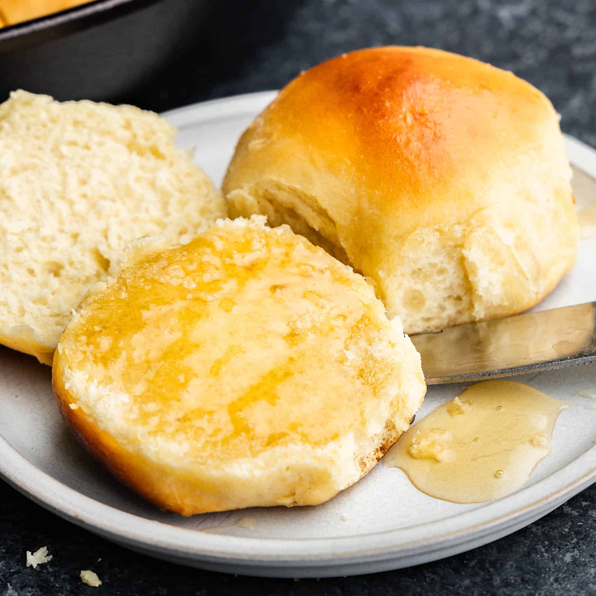 A plate holding skillet rolls, with one cut in half and the middle of it smothered in honey.