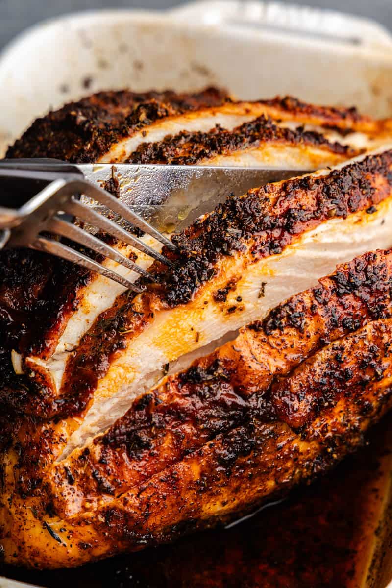 A Cajun-spiced roasted turkey breast in a roasting pan. A fork and knife showing you the cut interior.