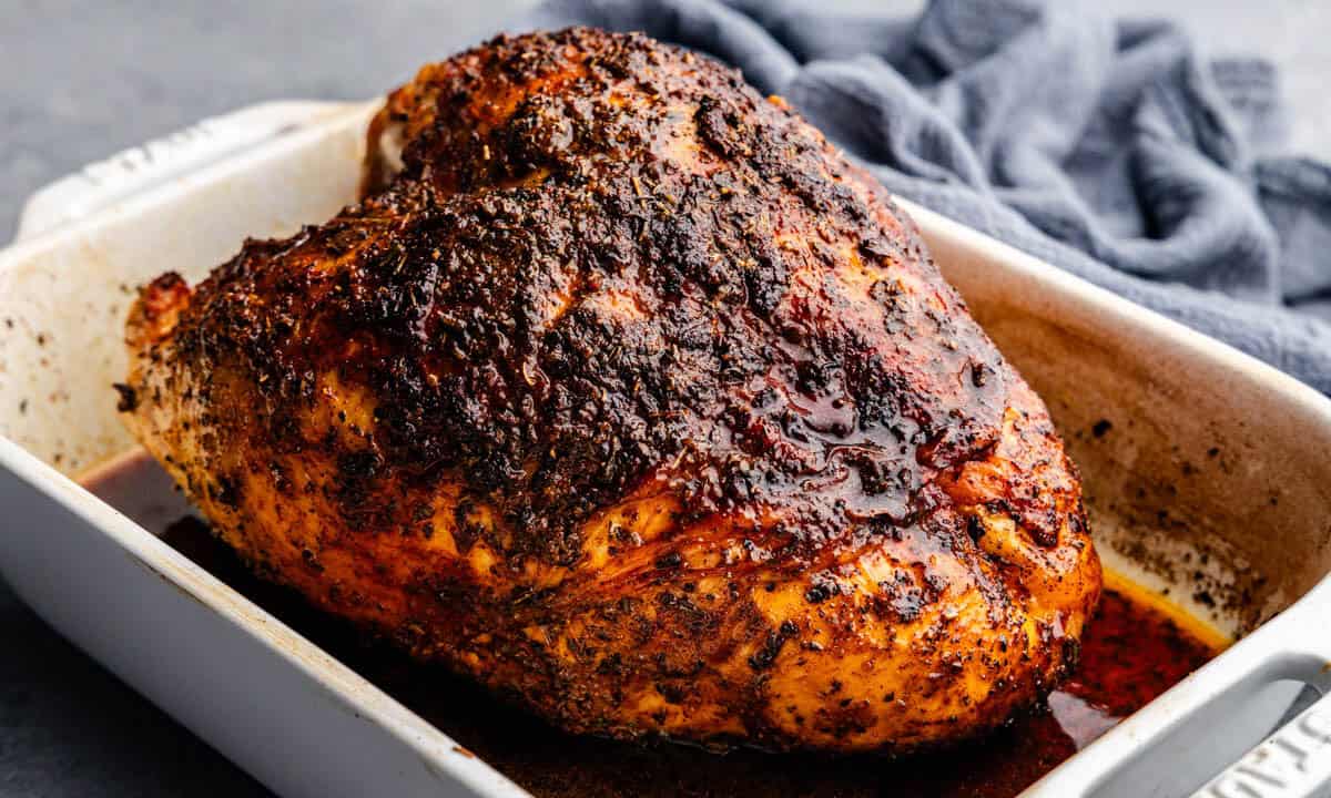 A roasted turkey breast in a white roasting pan. The turkey breast has been rubbed with cajun seasoning.