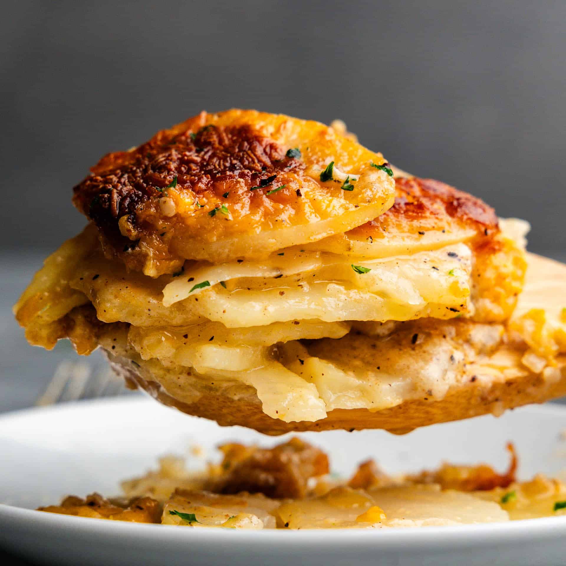 A helping of scalloped potatoes being scooped from the slow cooker and onto a white plate.