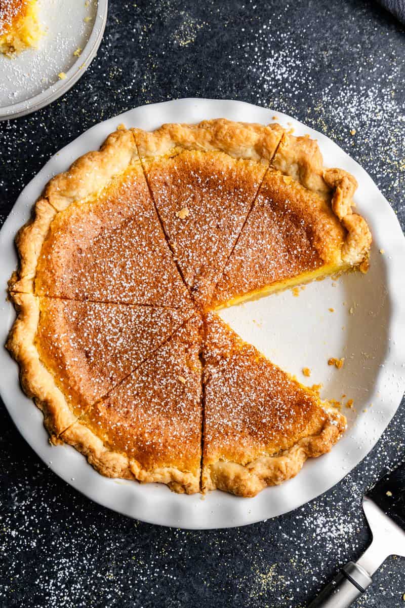 An overhead view of a chess pie that has been sliced for serving. The first slice has been removed from the pan.