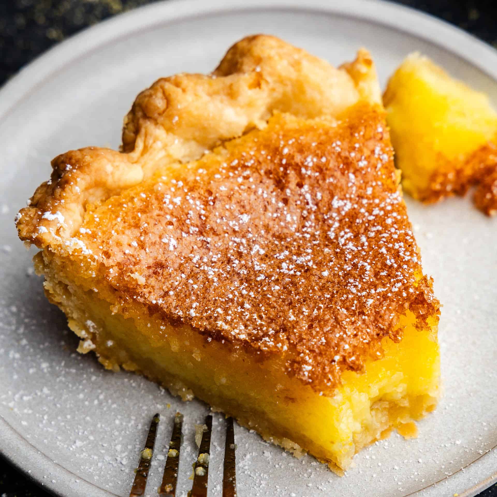 A close up view of a slice of chess pie on a plate with a bite taken out.