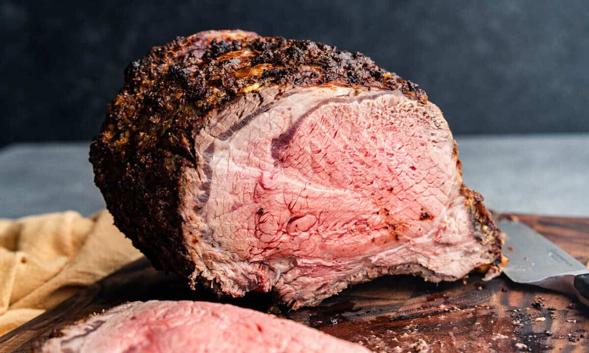 A bone-in horseradish crusted prime rib on a cutting board that has been sliced into to show the perfectly medium-rare interior.