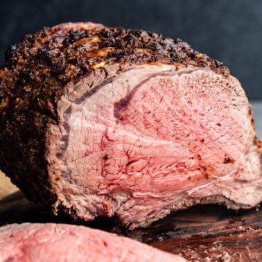 A bone-in horseradish crusted prime rib on a cutting board that has been sliced into to show the perfectly medium-rare interior.