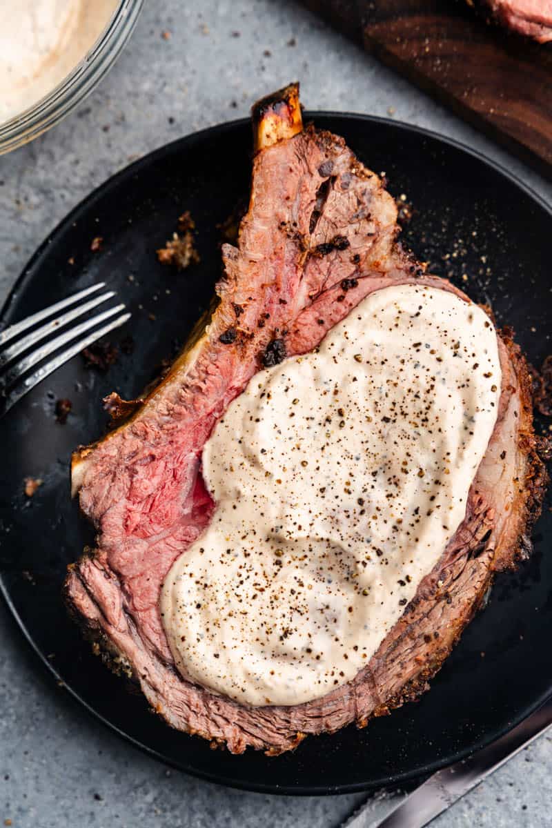 A blackened plate with slices of medium-rare prime rib smothered in a horseradish sauce.