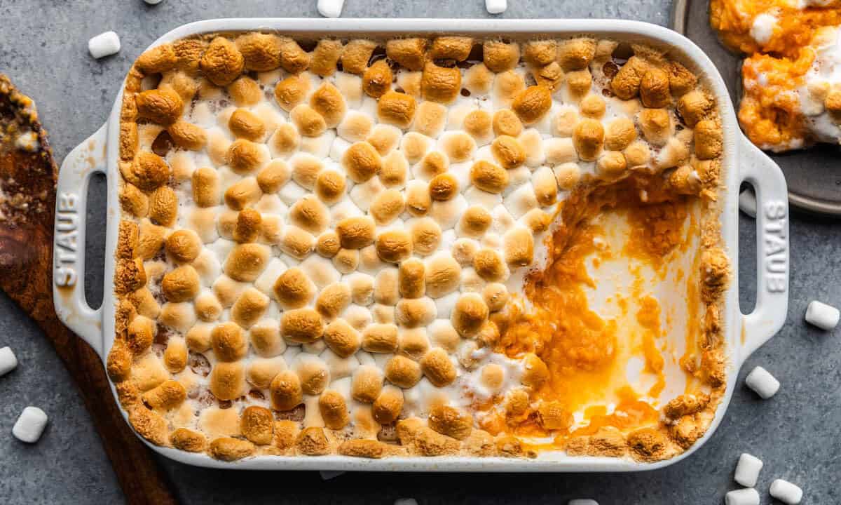 A pan of sweet potato casserole topped with toasted marshmallows. A large serving portion has already been removed.