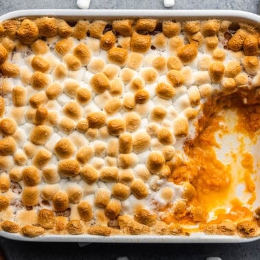 A pan of sweet potato casserole topped with toasted marshmallows. A large serving portion has already been removed.