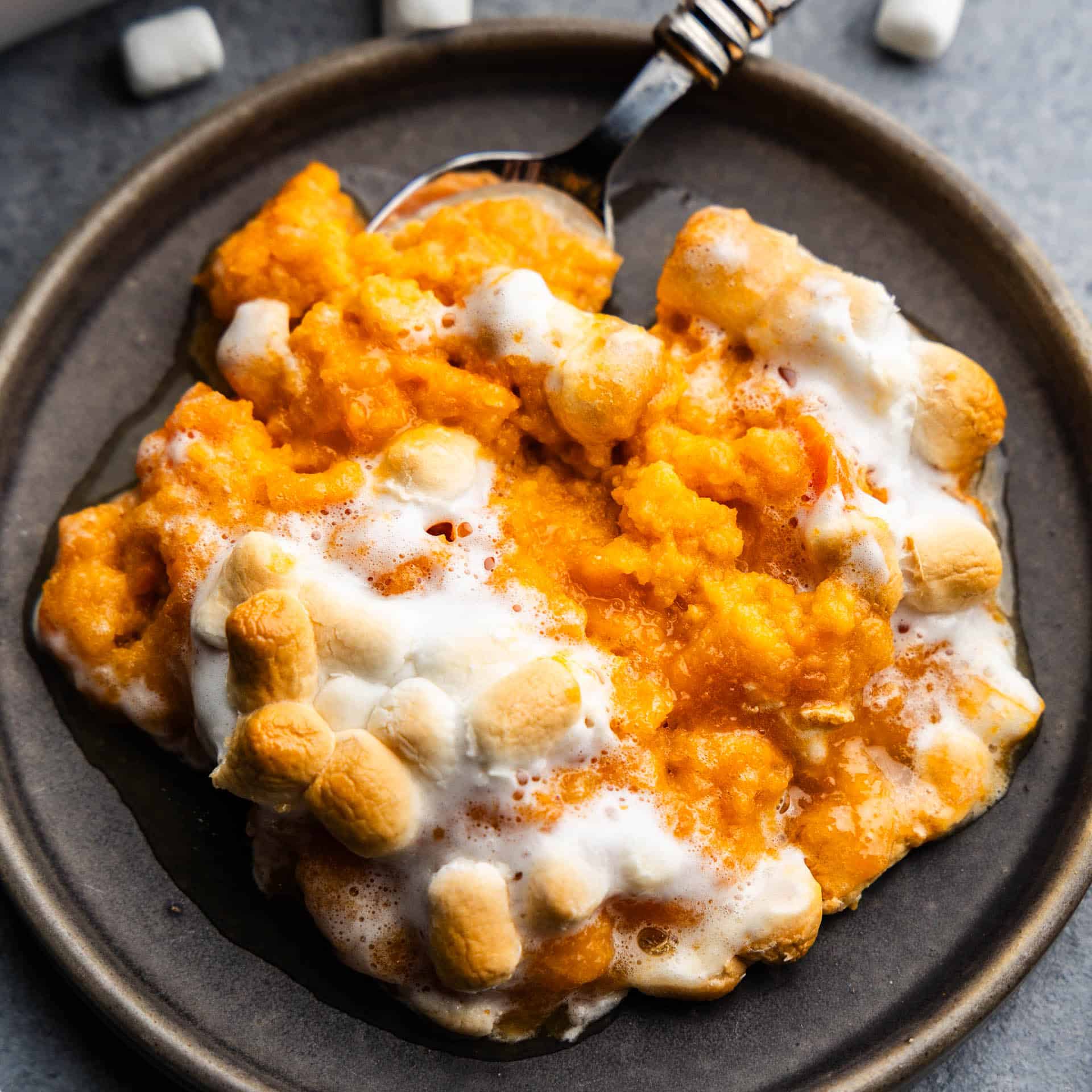 A plate holding a serving of sweet potato casserole with marshmallows with a spoon set in ready to eat.