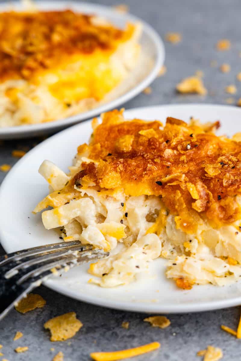 A serving of funeral potatoes on a white plate. A fork rested on the plate as if a bite had been taken from it.