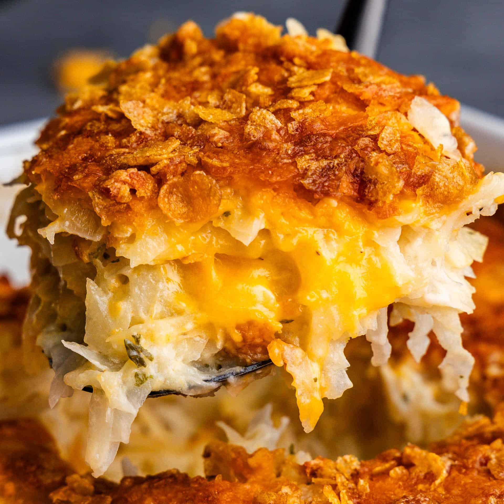 A helping of funeral potatoes being scooped out of the casserole dish.