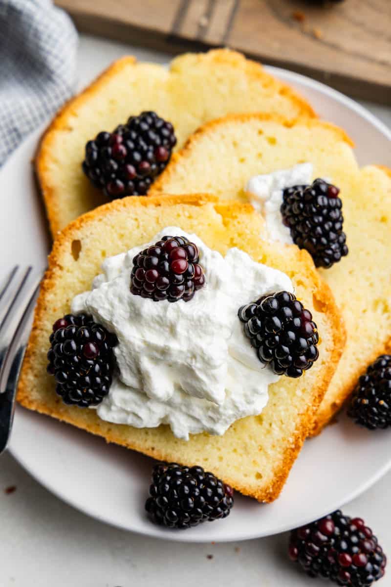 Slices of pound cake on a plate topped with whipped topping and blackberries