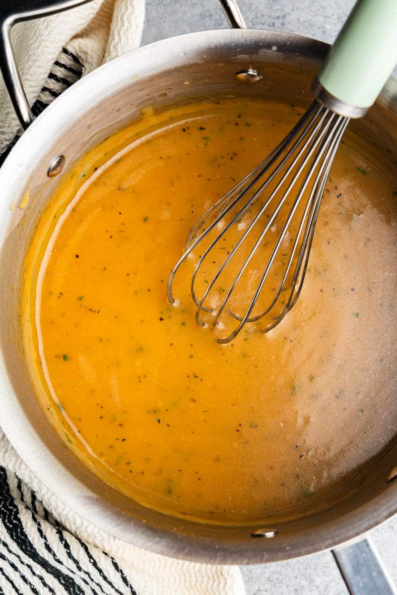 A whisk sitting inside pan of turkey gravy.