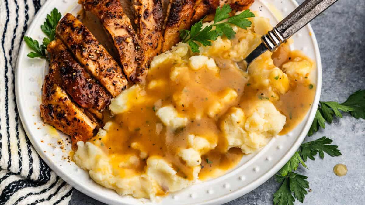 A close up view of a plate of mashed potatoes and turkey that has been drizzled with homemade turkey gravy.