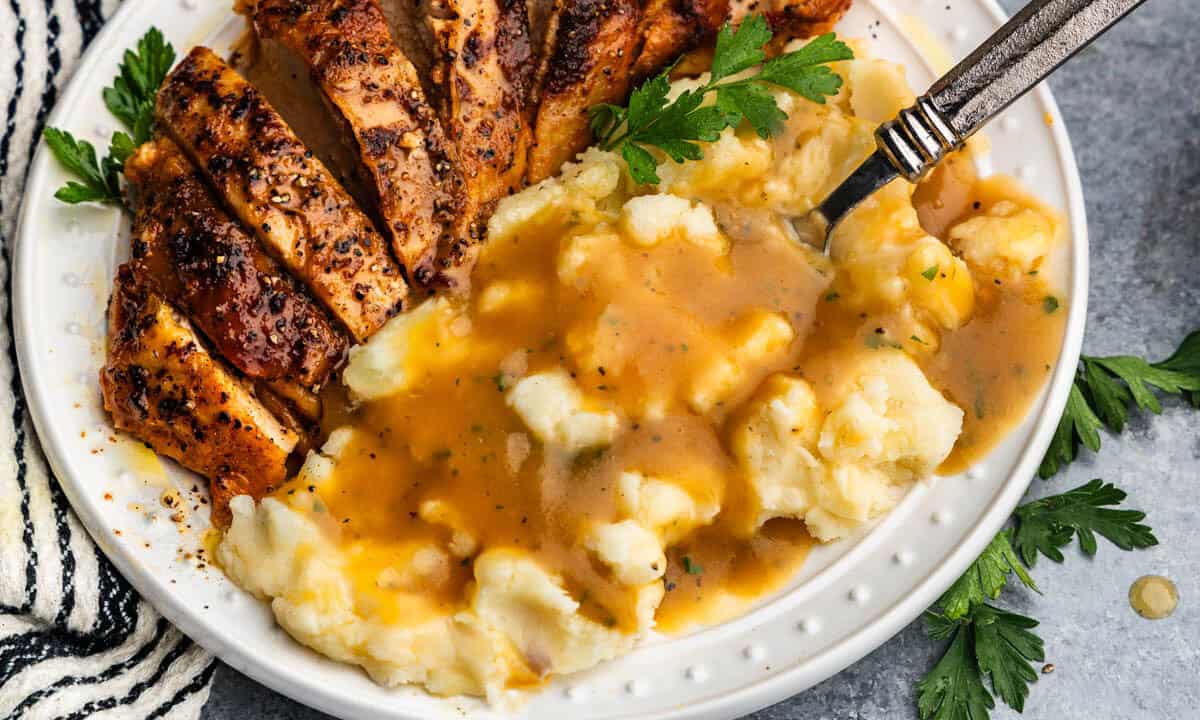 A close up view of a plate of mashed potatoes and turkey that has been drizzled with homemade turkey gravy.