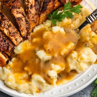 A close up view of a plate of mashed potatoes and turkey that has been drizzled with homemade turkey gravy.